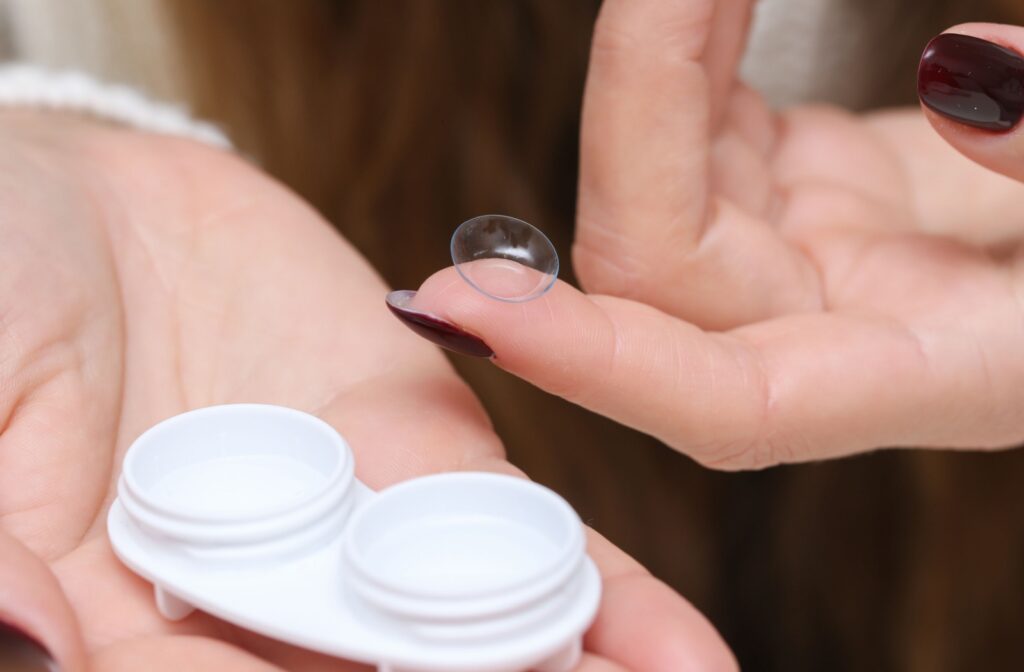 A person holds a contact lens near an open contact lens case while preparing to insert it