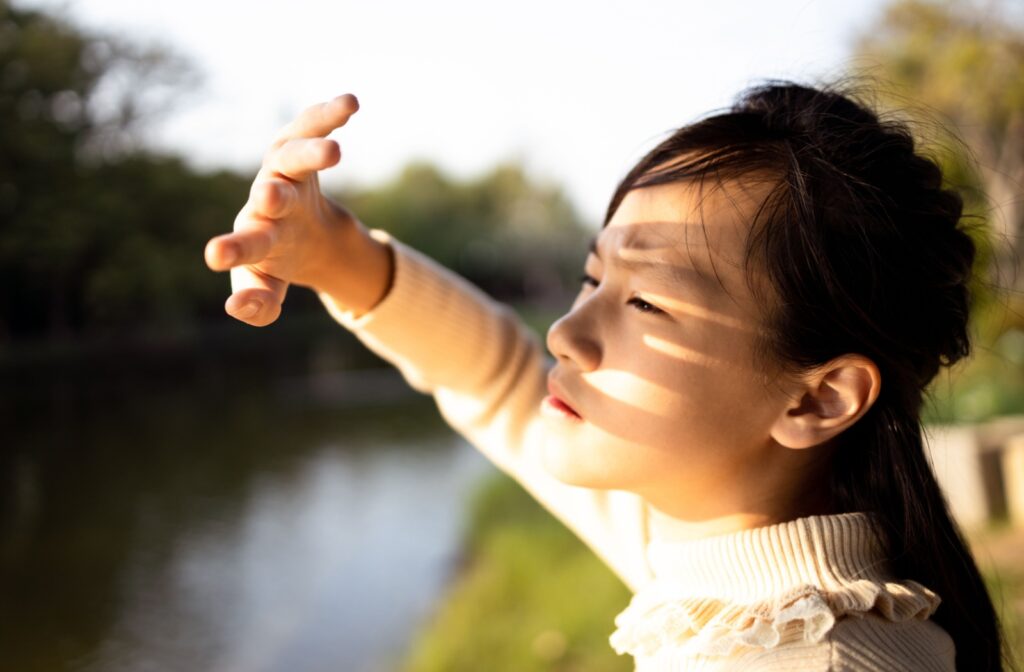 A person standing outside shields their eyes from the bright sun.