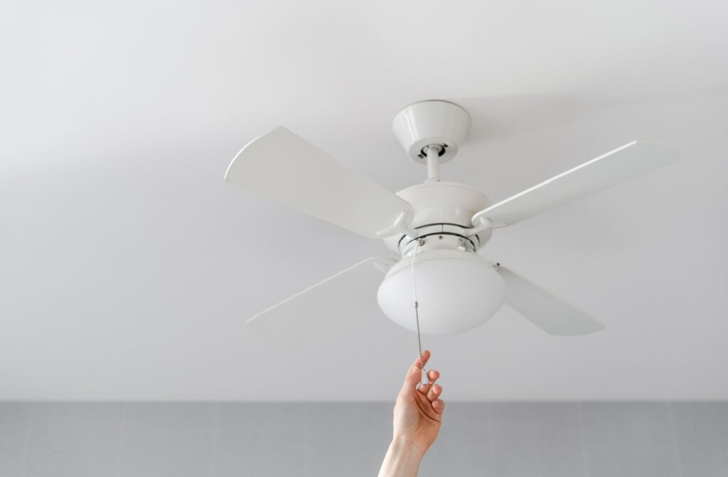 A hand reaching up to turn on a ceiling fan.