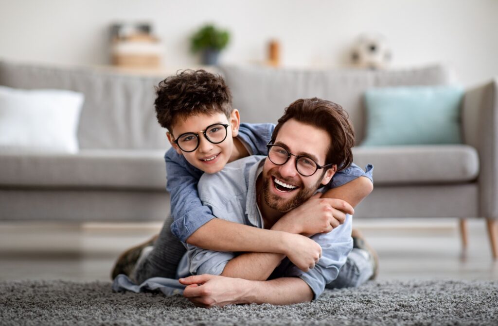 Parent and child happy on a rug: Child has arms around parent and both are lying on their front on a living room rug.