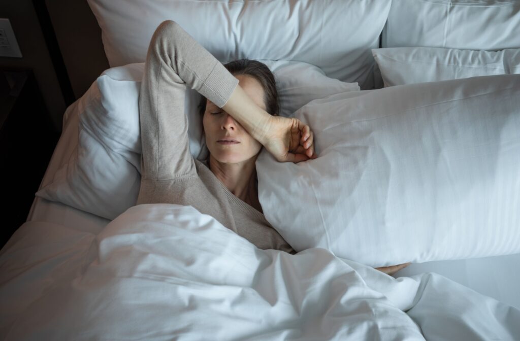Woman laying in bed with her arms over her eyes as she wakes up