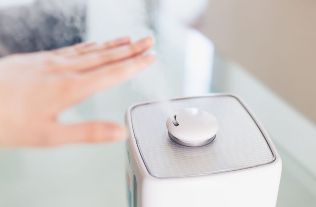 A hand touching the mist that is coming out of a white humidifier.
