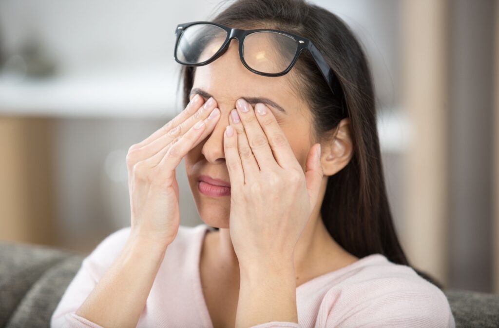 A person with their glasses lifted on their forehead so they can rub their dry and irritated eyes
