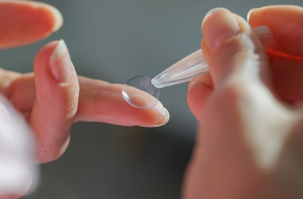 A close up of a contact lens on a finger being picked up using contact lens tweezers
